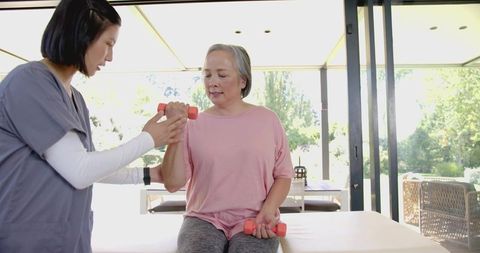 Senior woman receiving guided arm rehabilitation with therapist using coral dumbbells