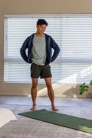 Young asian man standing on yoga mat at home preparing for morning workout routine