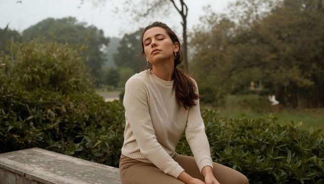 Serene young woman sitting on stone bench with eyes closed in leafy park