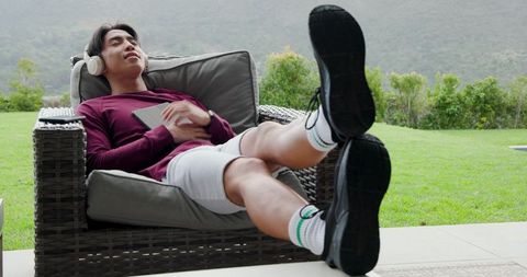 Asian Man Relaxing on Patio Lounger with Headphones and Tablet