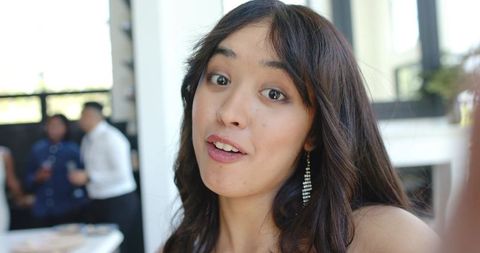 Young woman taking selfie and speaking at lively indoor party wearing rhinestone earring