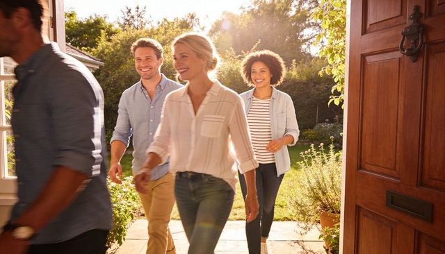 Friends entering sunlit home through open doorway, casual garden gathering arrival welcome