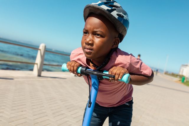 African american boy wearing helmet leaning on push scooter at promenade on sunny day - Download Free Stock Photos Pikwizard.com
