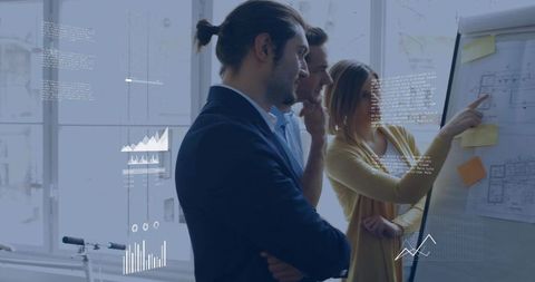 Collaborating team reviewing blueprints and data on flip chart in sunlit modern office