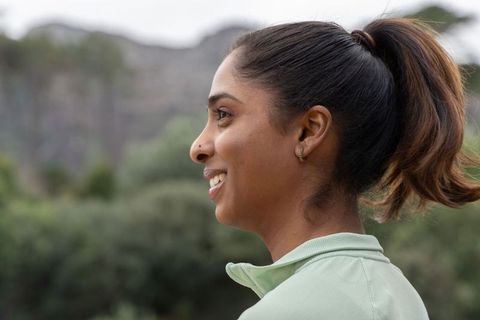 Smiling indian woman enjoying nature trail wearing light green zip-top with ponytail