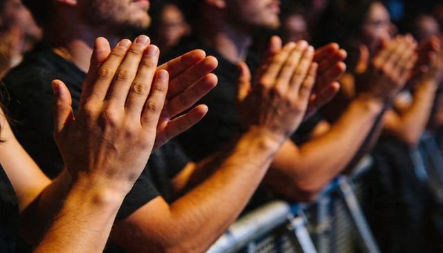 Clapping crowd front row close-up showing hands on barrier under dramatic concert lighting