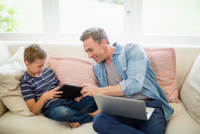 Father and son using laptop and digital tablet in living room at home