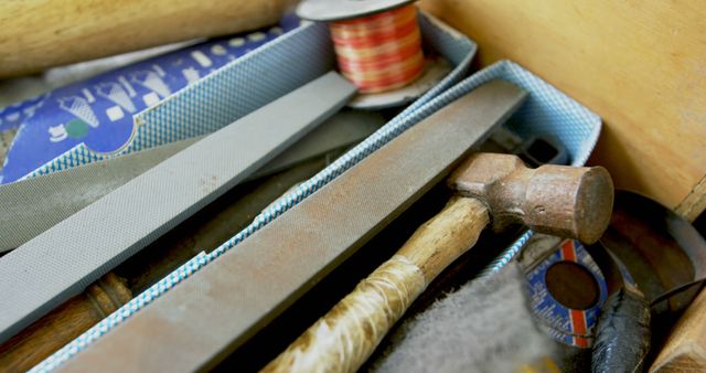 A close-up view of a collection of tools and hardware items, including a hammer, files, and spools of thread, with copy space. These items suggest a workspace where crafting or repair work might be undertaken.