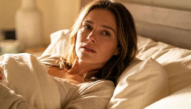 Woman reclining in cozy bed wearing light sweater and lace camisole, warm intimate morning