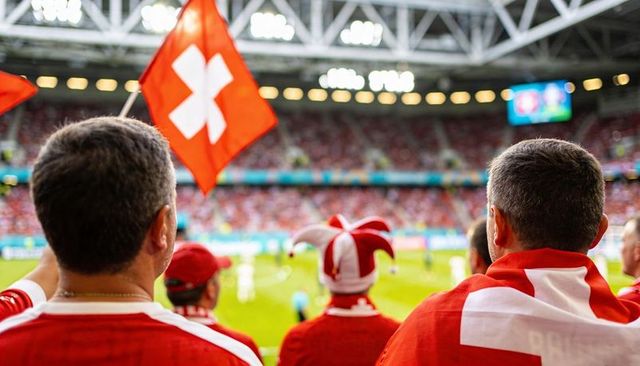 Cheering swiss supporters waving national flag in packed stadium, celebrating football matchday