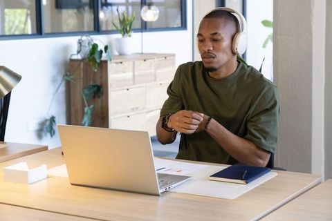 African american man wearing headphones working on laptop in modern minimalist home office