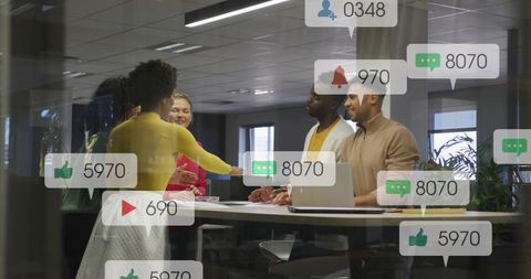Diverse team collaborating at table with social media notifications and handshake