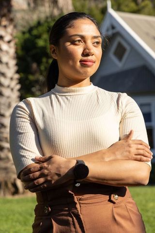 Confident asian woman standing with arms crossed in sunlight on suburban lawn