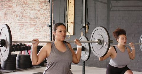 Women training barbell back squats in industrial gym, teamwork strength and focus