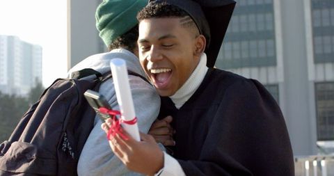 African american graduate celebrating with friend hugging on campus holding diploma