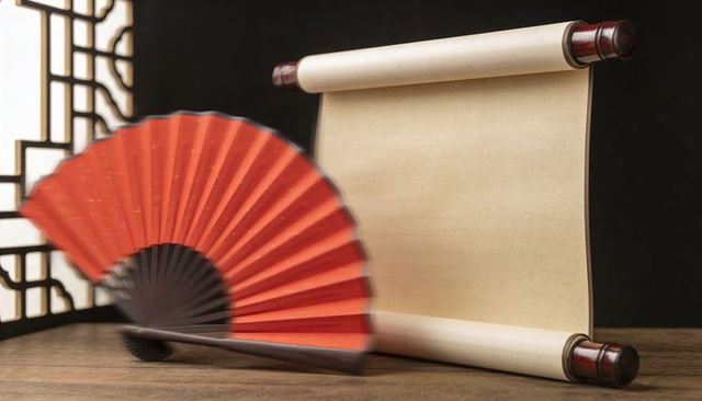 Displaying blank parchment scroll with red folding fan and lattice panel on wooden tabletop