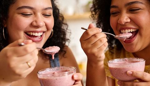 Laughing friends enjoying pink yogurt bowls together in cozy kitchen closeup