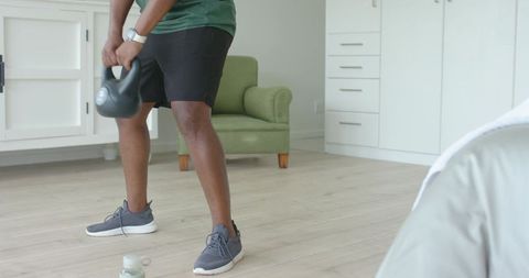 African american man performing kettlebell swing in bright minimal living room