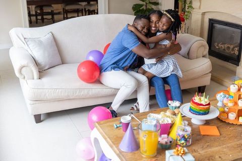African american family hugging on sofa celebrating rainbow birthday party at home