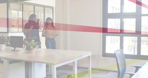 Colleagues discussing plans walking past glass meeting room in modern open-plan office