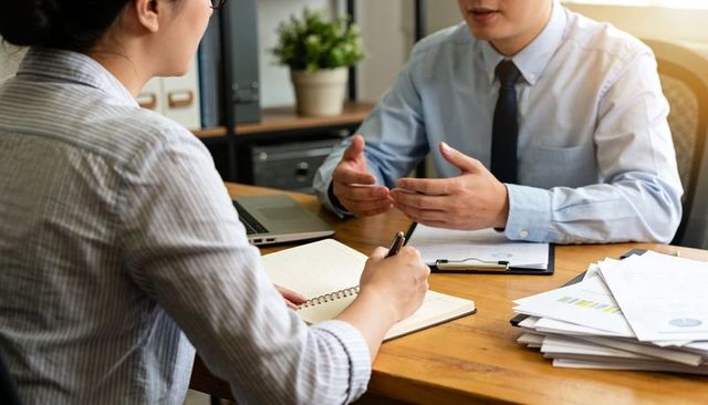 Manager explaining while colleague taking notes during office meeting and report review