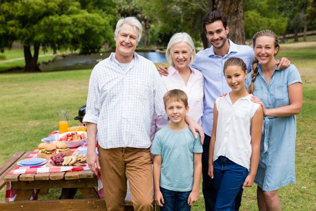 Multigenerational family enjoying time together in a park, posing for a group photo. Ideal for use in advertisements, family-oriented content, and promotional materials for outdoor activities or family gatherings. Highlights themes of togetherness, happiness, and nature.