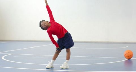 Young Boy Stretching on Basketball Court in Athletic Outfit