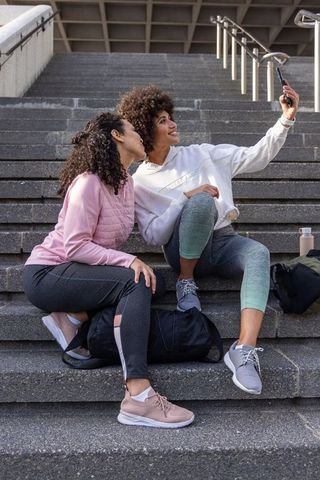 Two friends taking selfie on city steps after workout, casual athletic urban lifestyle
