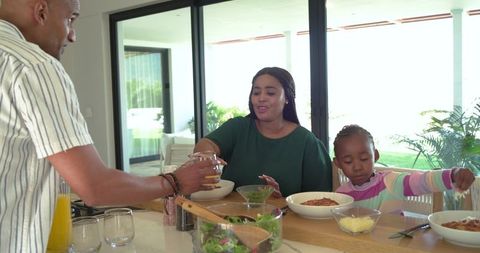 African american family sharing pasta at kitchen island while dad pours juice at mealtime