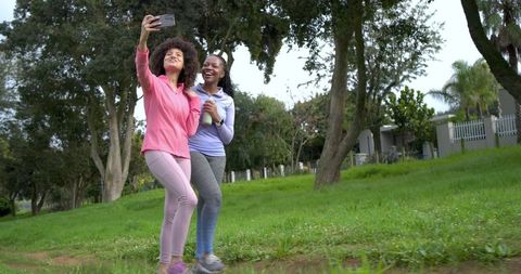 Diverse female friends taking selfie on park trail during morning activewear walk