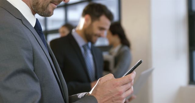 Business professionals engaging on a smartphone in an office setting. Ideal for images representing corporate communication, modern business technology, and professional work environments. Suitable for marketing materials, business presentations, and articles on business trends.