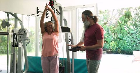 Senior Woman Stretching with Personal Trainer in Home Gym