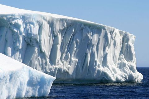 Massive Tabular Iceberg Towering Over Deep Blue Polar Ocean With Sheer Ice Cliff