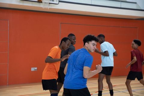 High-energy teen athletes sprinting and defending during indoor basketball drill, teamwork