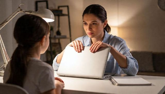 Evening parent closing laptop to set screen time boundary with child at cozy desk