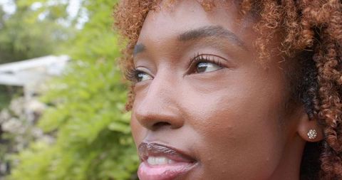 African american woman enjoying garden sunlight with glossy lips and sparkly stud earring