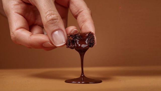 Pinching manicured hand holding fudgy brownie, glossy ganache dripping and pooling