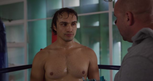 Young boxer in gym receiving guidance from his experienced trainer. Both are engaged in a serious conversation. Ideal for use in promotions for sports, fitness training, boxing gear, motivational content for athletes, or advertisements.