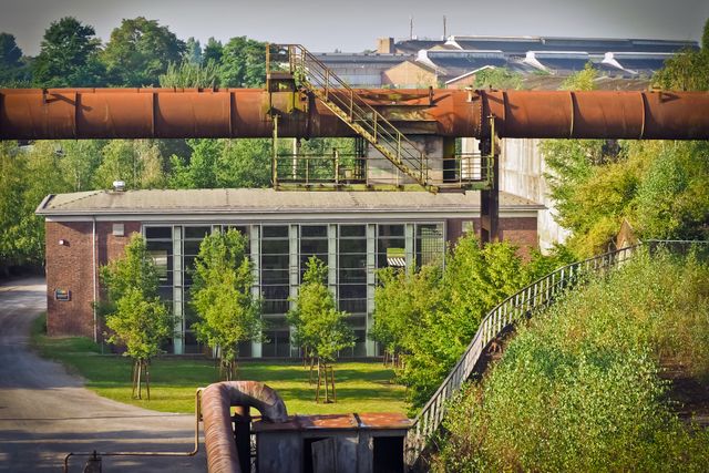 Old Industrial Building with Rusty Structures and Green Surrounding Trees - Download Free Stock Images Pikwizard.com