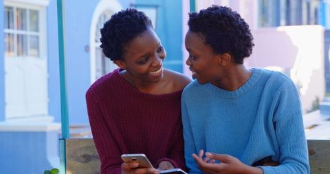 African American Sisters Smiling and Using Smartphone Outside