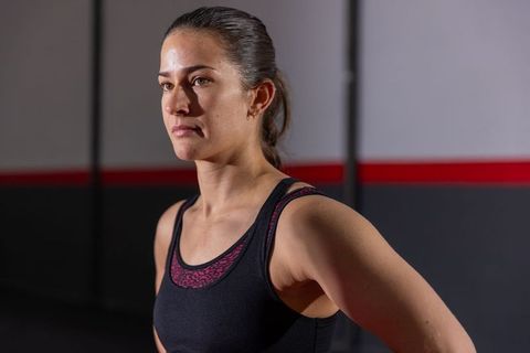 Female athlete standing arms akimbo in gym with focused determined expression