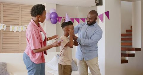 African american parents placing purple party hat on son during birthday celebration