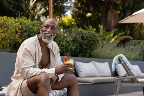 Mature man smiling and relaxing poolside holding tropical drink garnished with strawberry