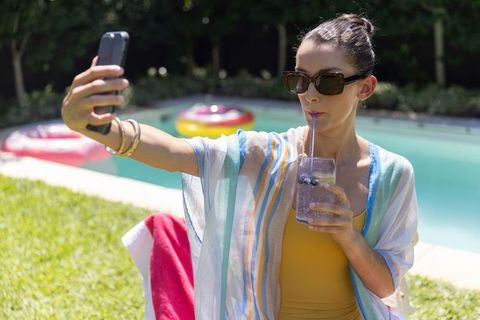 Poolside selfie sipping citrus spritzer, relaxing in swimsuit and sunglasses, summer backyard vibe