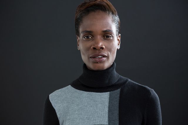 This image features an androgynous man wearing a black and grey turtleneck sweater, standing against a grey background. The serious and confident expression makes it suitable for use in fashion editorials, modern style blogs, and articles discussing gender identity and androgyny. The neutral background allows for easy integration into various design projects.
