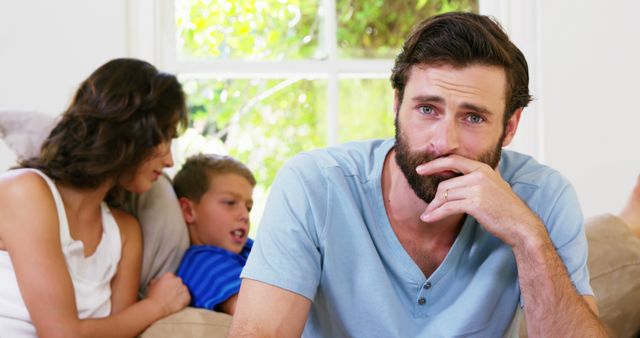 Stressed Man Sitting on Couch with Family in Background - Download Free Stock Images Pikwizard.com