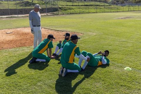 Baseball teammates stretching on grass before game with coach observing