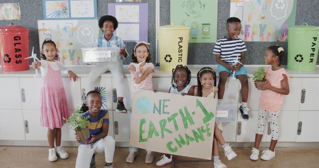 Group of cheerful children promoting recycling and environmental awareness by holding recycling bins and plants. They stand beside labeled recycling bins for glass, plastic, and paper, displaying a sign that reads 'One Earth - One Chance'. This image can be used for campaigns promoting sustainability, environmental education in schools, eco-friendly initiatives, and community engagement projects.