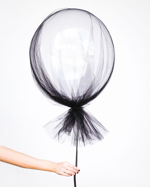 Hand holding a balloon covered in black tulle against white background. The minimalist and elegant design makes it great for birthday parties, celebrations, invitations, or decor ideas. Ideal for use in artistic, fashionable promotional materials or for special events decoration inspiration.