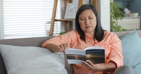 Mature woman reading book on sofa at home turning page calm relaxed lifestyle moment